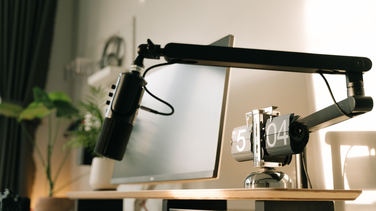 A sleek and modern workspace featuring a microphone and flip clock on a wooden desk setup.