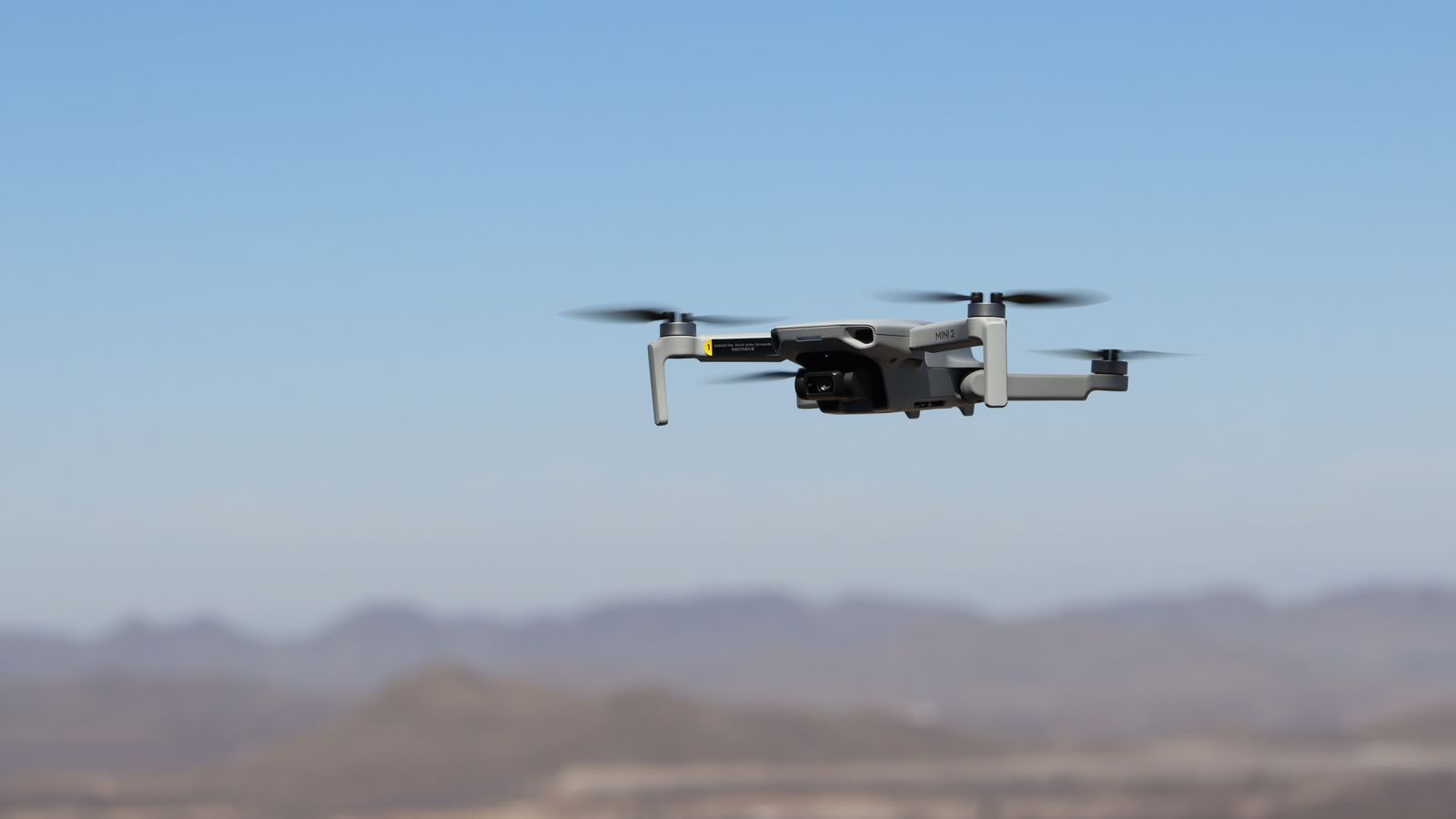 Drone flying over a desert landscape under clear blue skies.