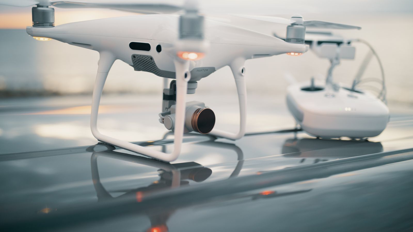 A close-up view of a sleek drone with its controller on a reflective surface during sunset.