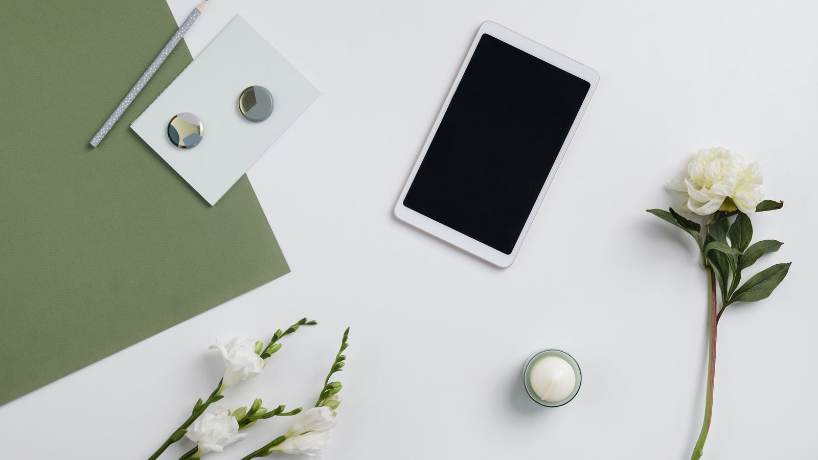 Minimalist composition featuring a tablet, flowers, and stationery on a white background.