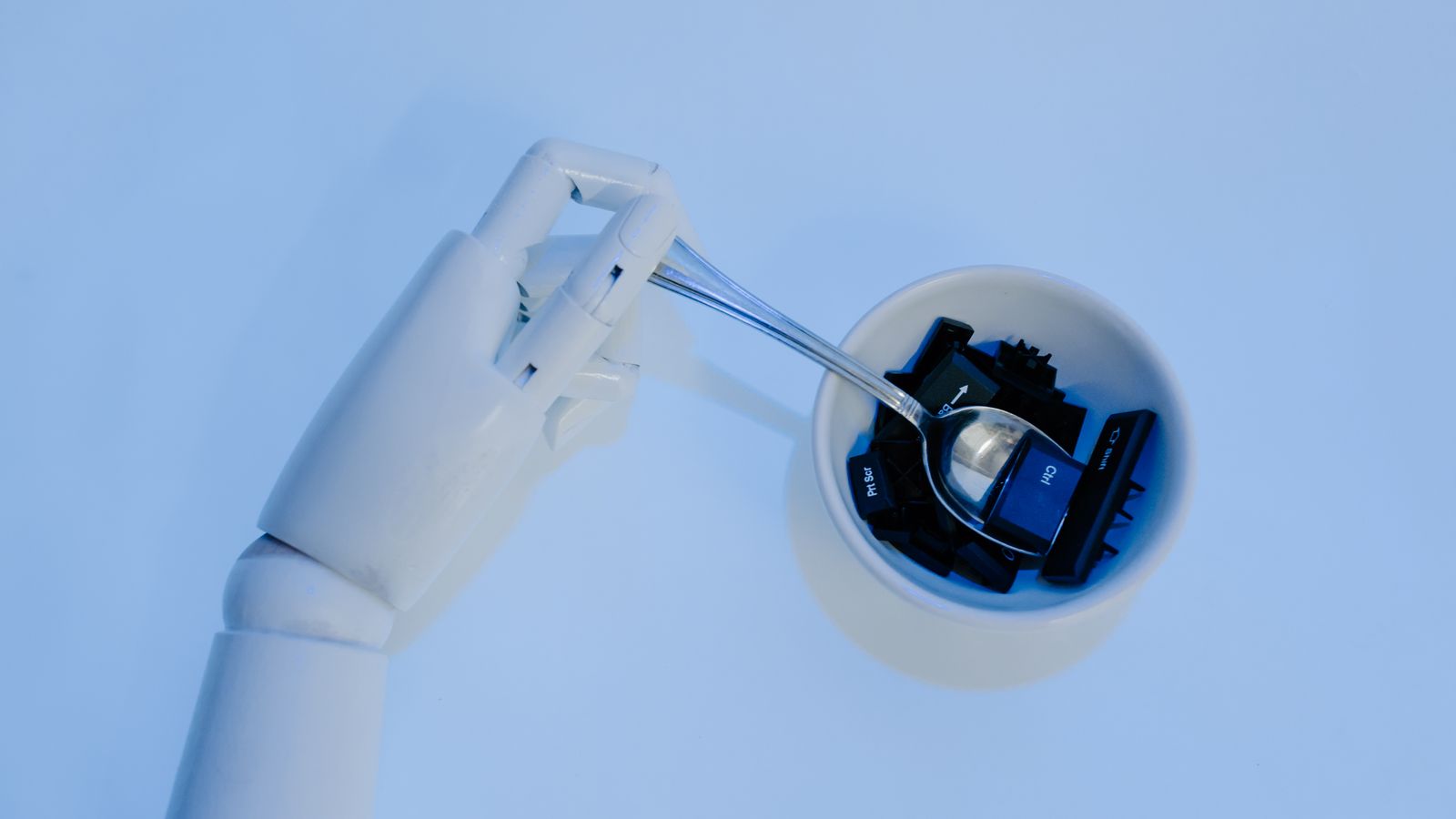 A robotic hand holds a spoon filled with keyboard keys, symbolizing AI and technology fusion.