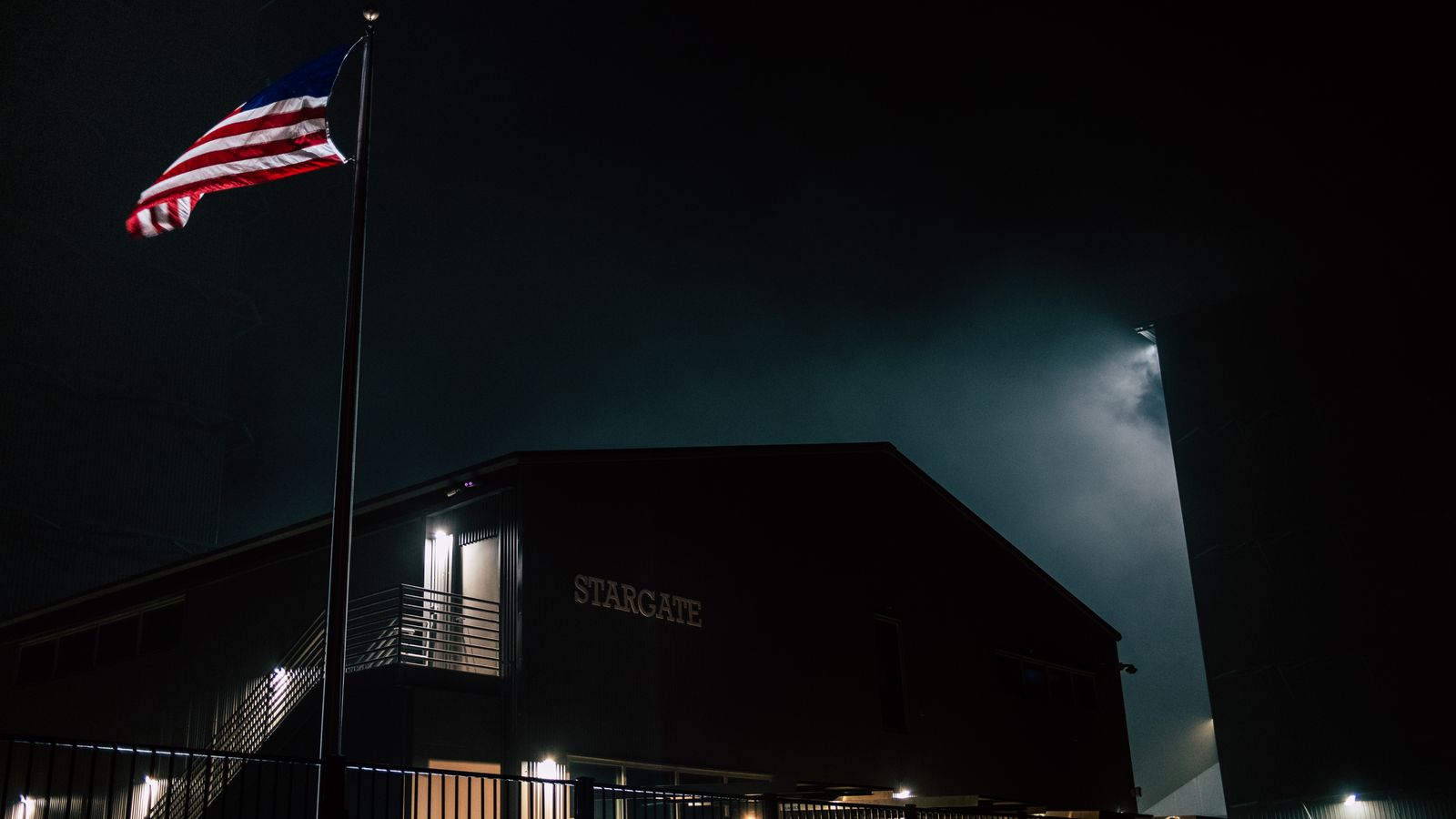 Dark atmospheric view of the Stargate building with an American flag at night.