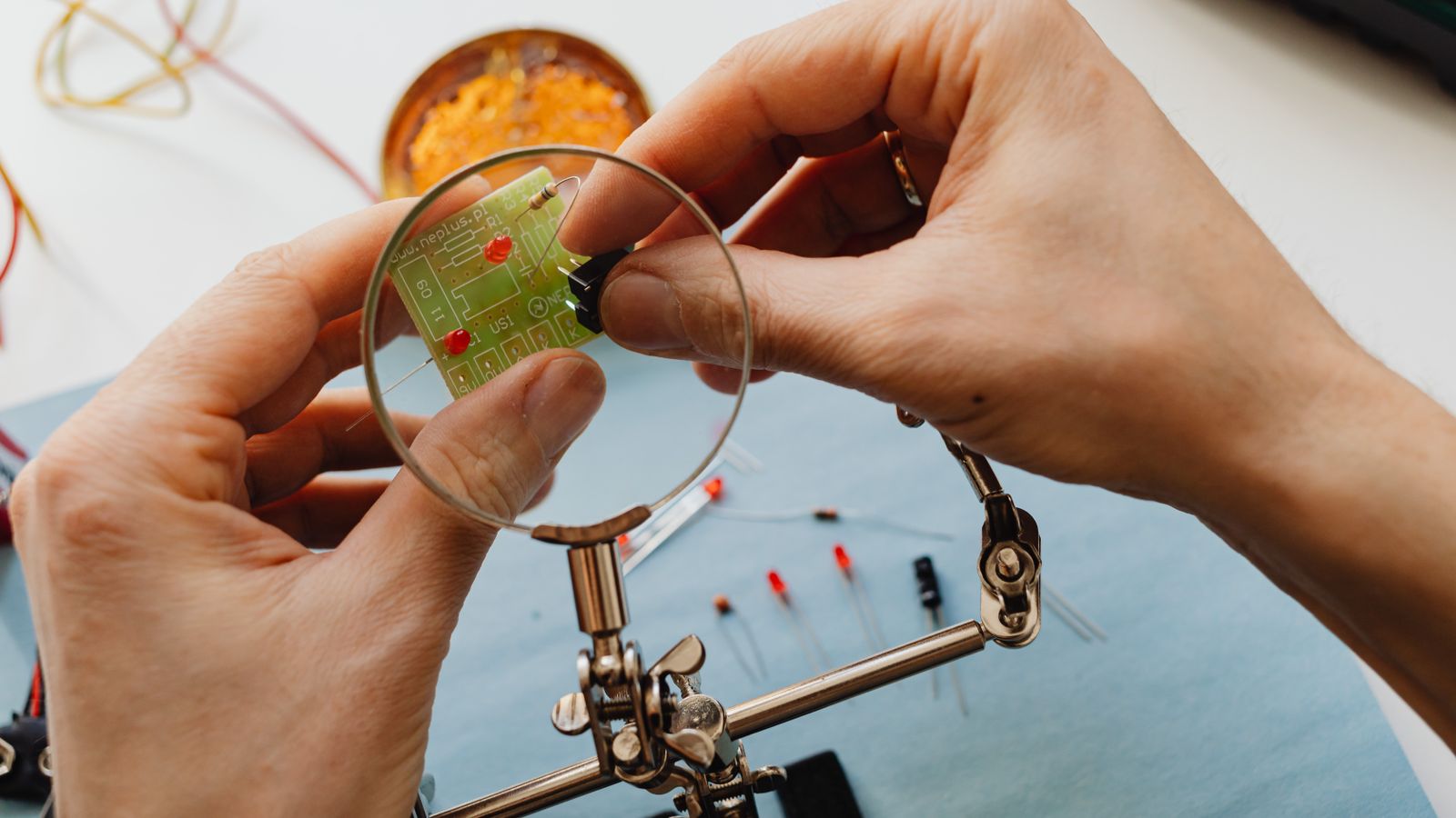 Close-up of hands using a magnifier to work on a circuit board with electronic components.