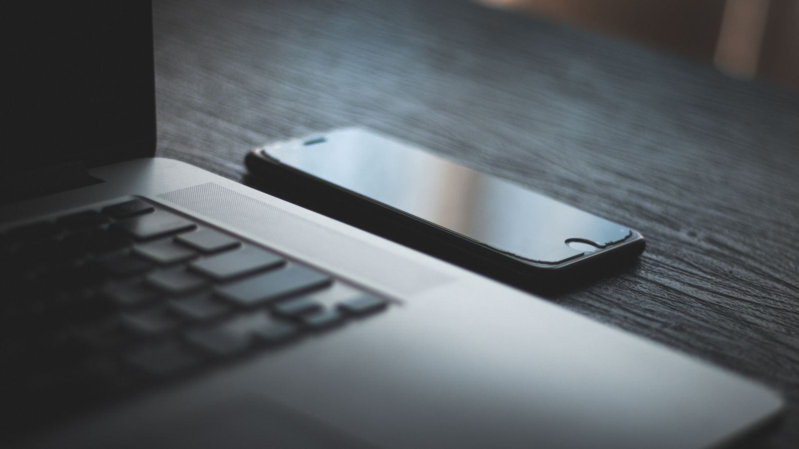 Modern laptop and smartphone on a textured wooden desk, capturing the essence of contemporary technology.