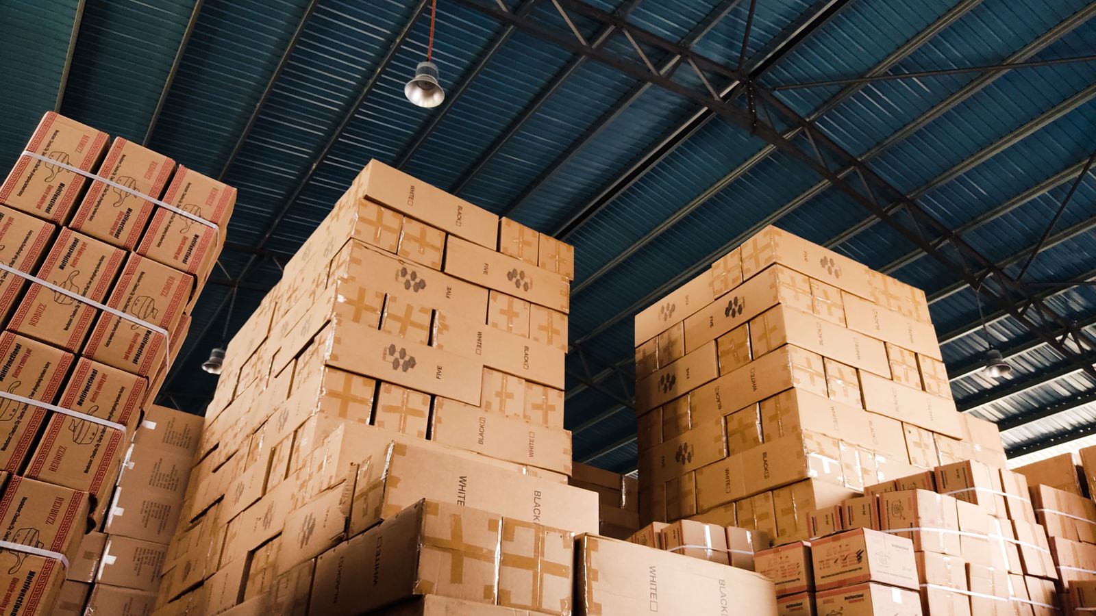 High stacks of cardboard boxes organized in a warehouse with a blue metal ceiling.