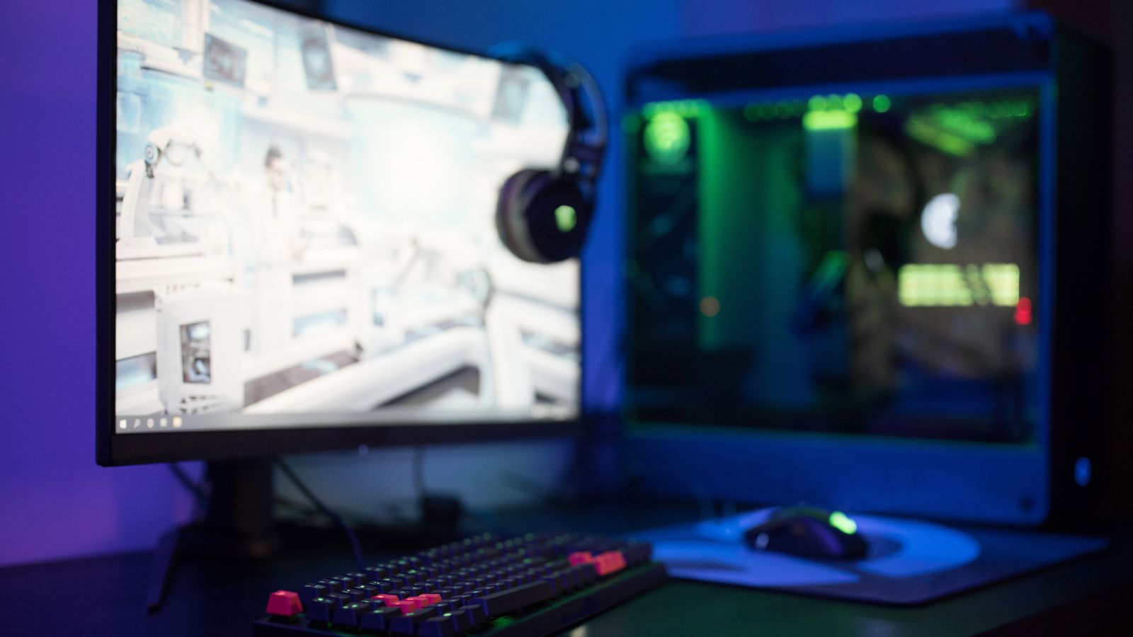 High-tech gaming setup featuring a curved monitor, RGB keyboard, and vibrant lighting.