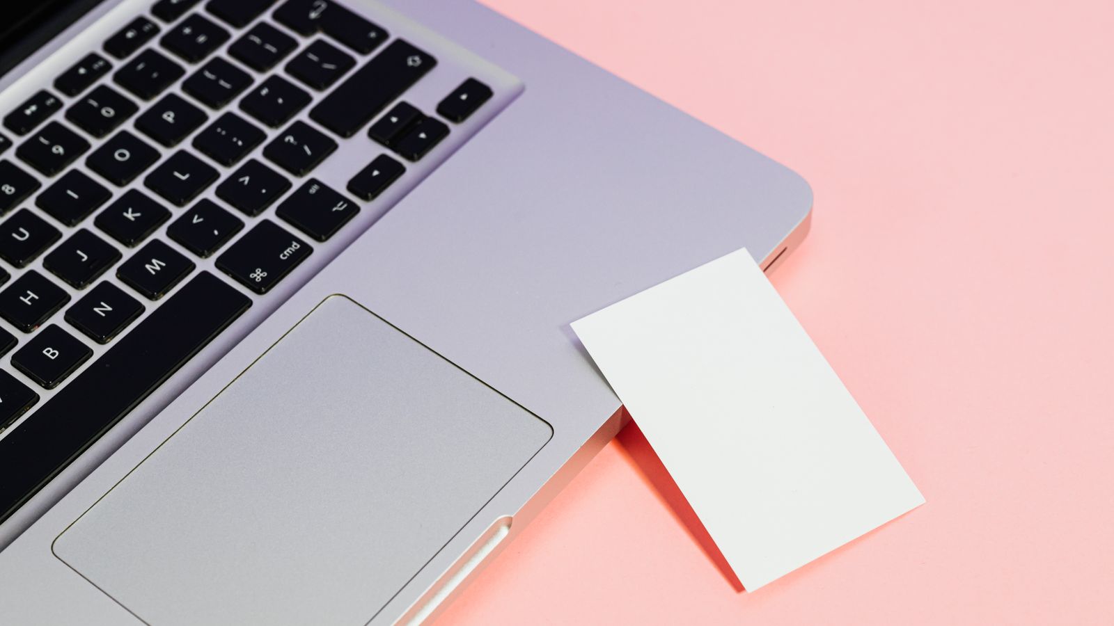 Close-up of a laptop with a blank card on a pink background, ideal for tech concepts.