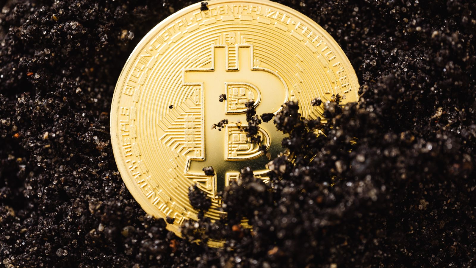 A gold Bitcoin coin partially buried in dark soil symbolizing digital currency growth.