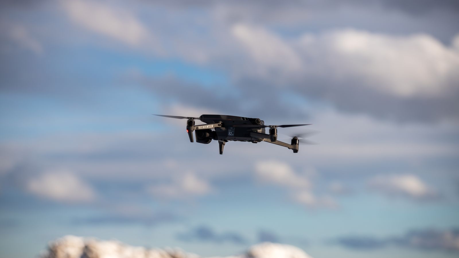 Aerial view of a drone flying over snow-covered mountains with dramatic clouds.
