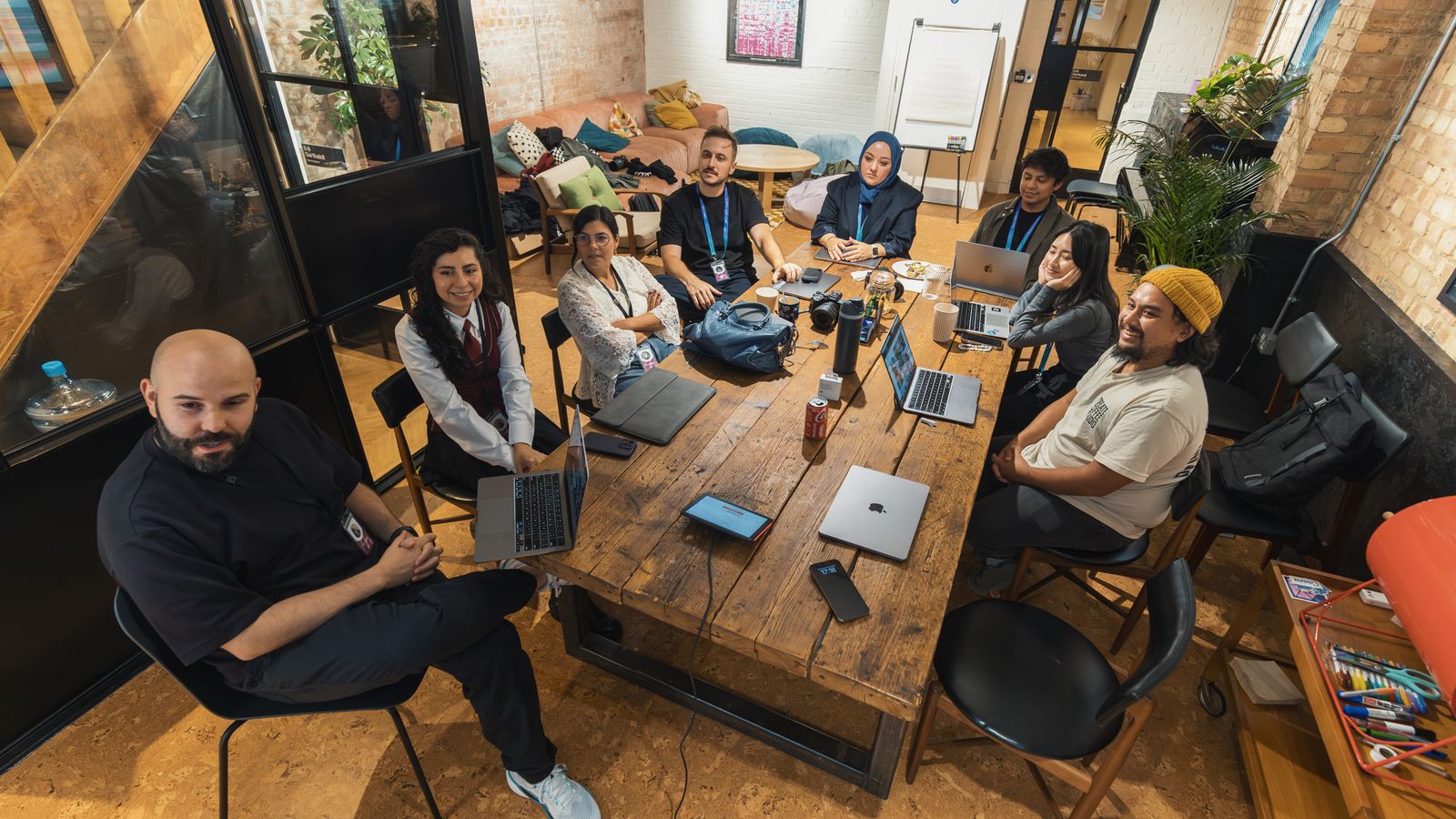 Group of colleagues gathered around a table in a modern office setting, collaborating on laptops.