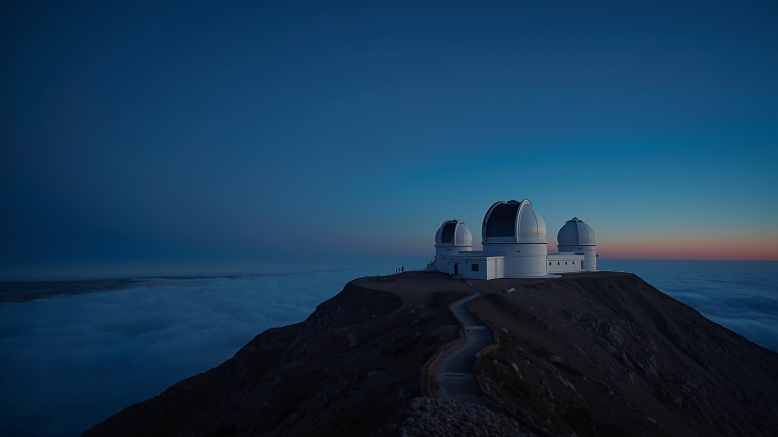 Observatory domes on a summit above clouds at blue hour