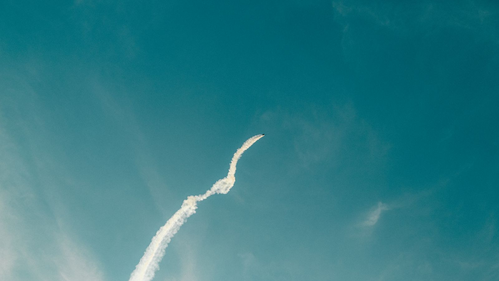 Aerobatic airplane leaves a white smoke trail against a clear blue sky, showcasing dynamic flight patterns.