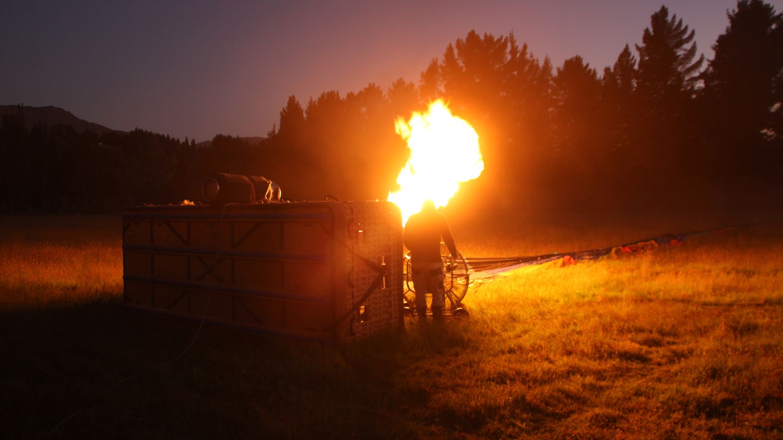 A hot air balloon being prepared with fire at dusk in a field, creating a dramatic glow.