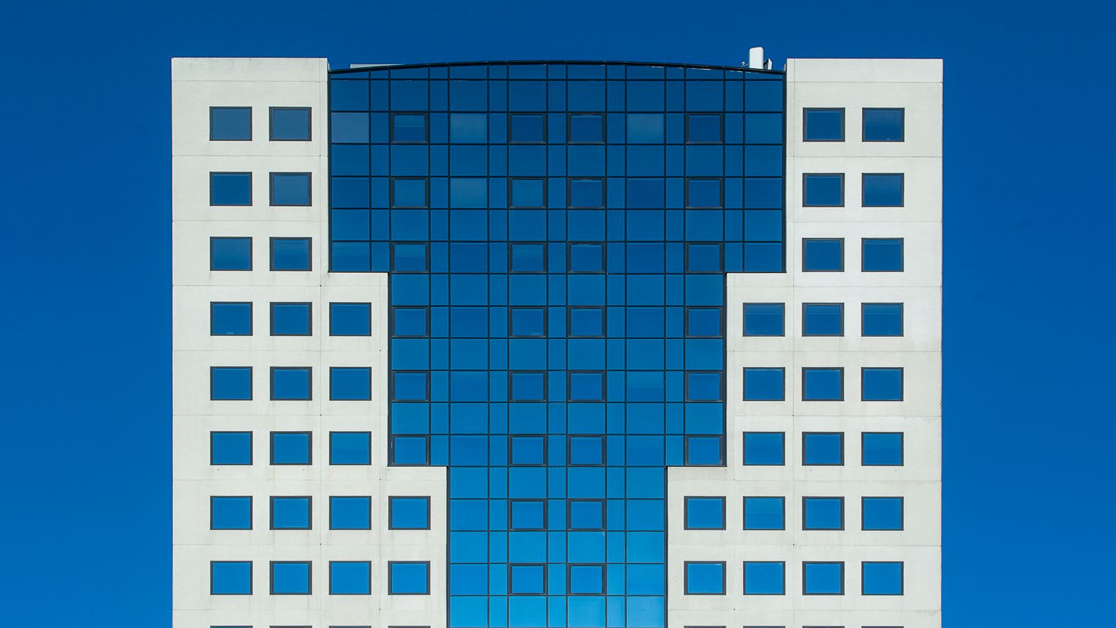 A modern office building featuring a striking geometric facade against a clear blue sky.