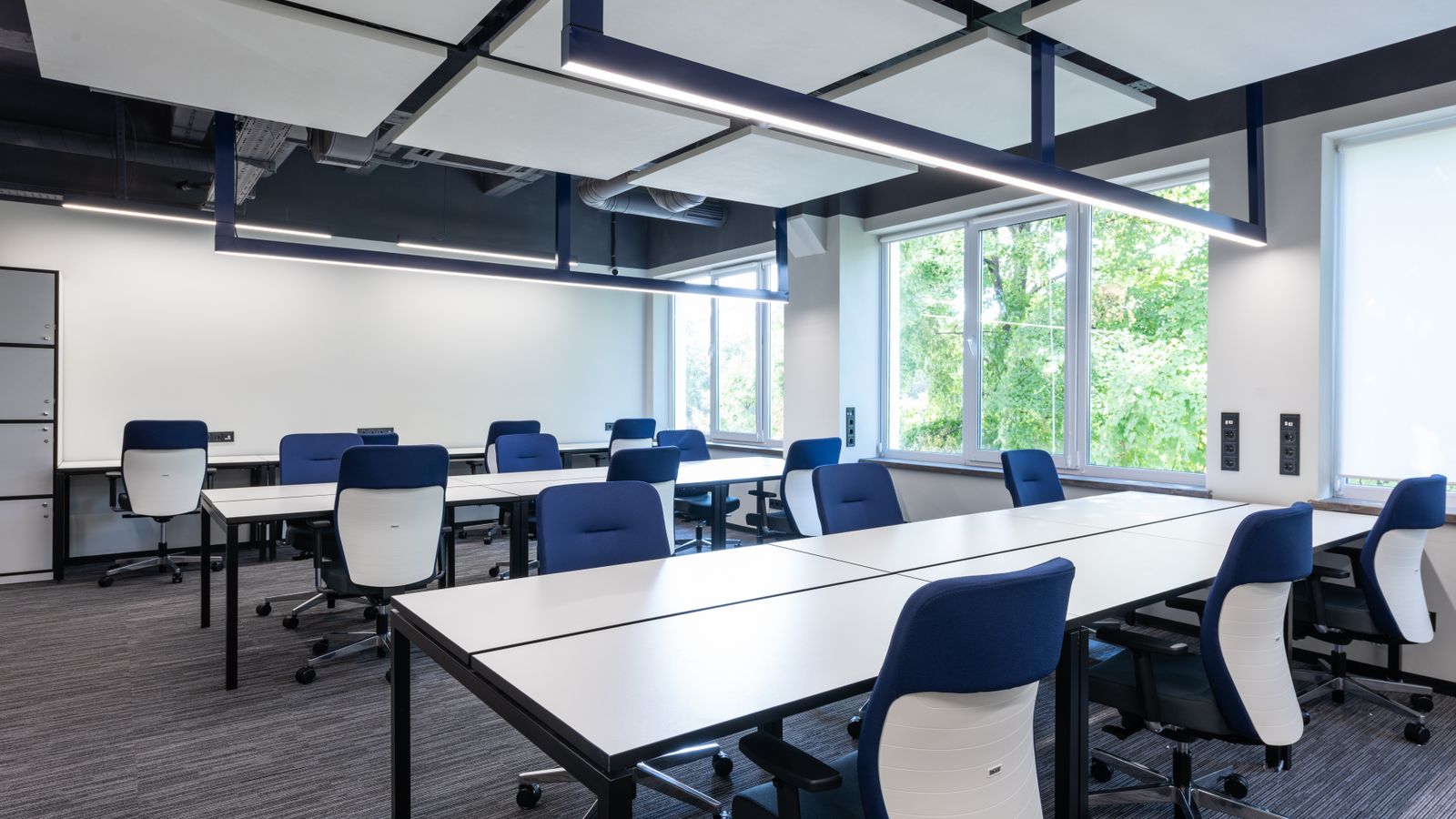 White long tables with comfortable blue armchairs placed in spacious open space office with big window in modern business center