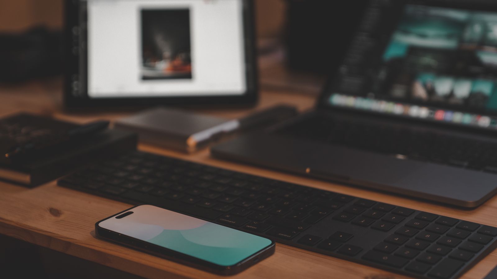 A contemporary workspace setup featuring a laptop, smartphone, and tablet on a wooden desk.