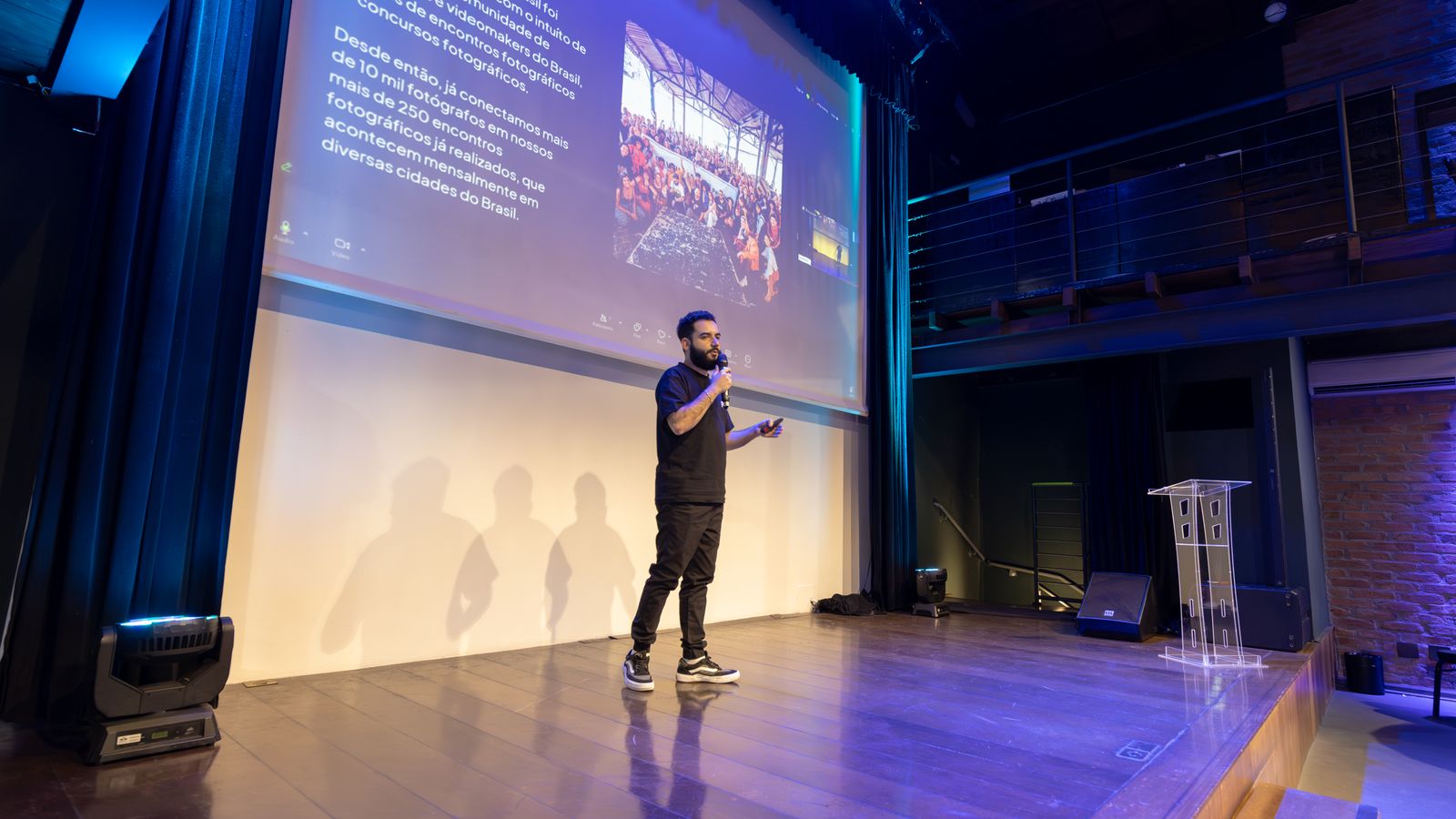 Speaker presenting at a conference with a projected presentation slide on screen.