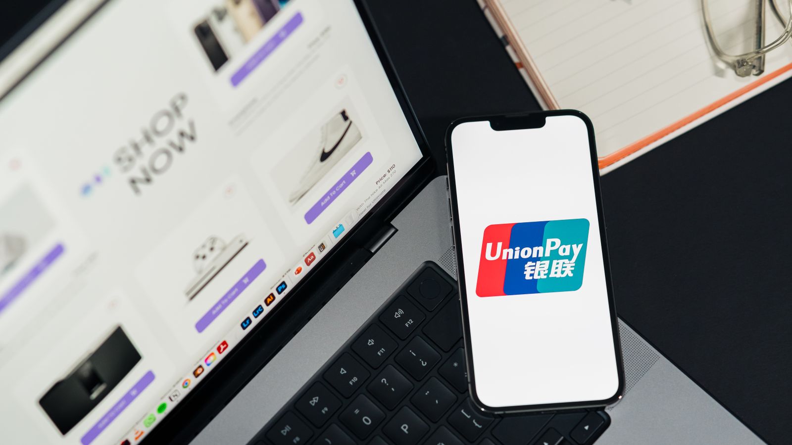 UnionPay logo displayed on a smartphone next to a laptop with an online shopping page open.