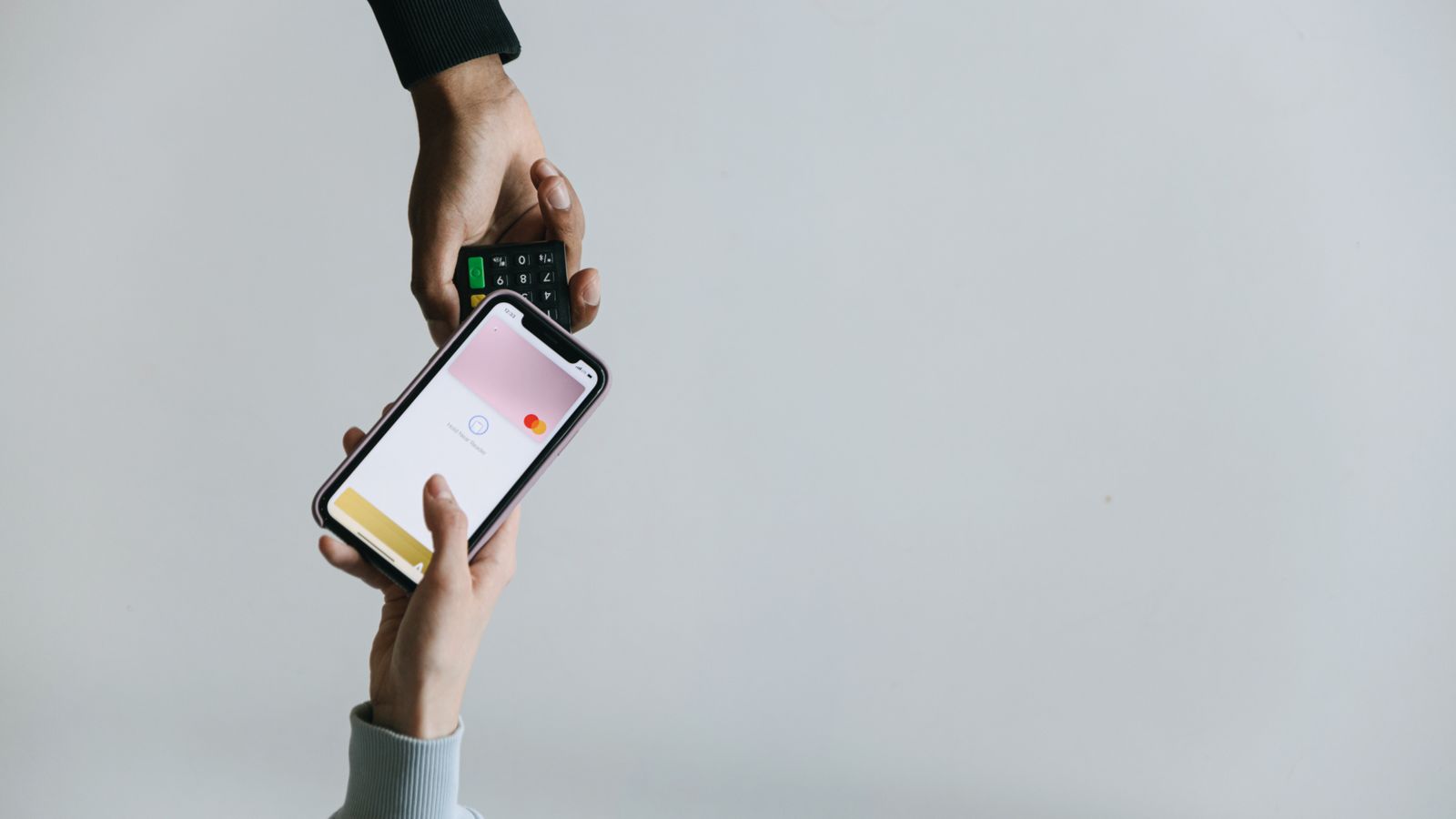 Hands using smartphone and terminal for cashless payment, showcasing modern transaction methods.