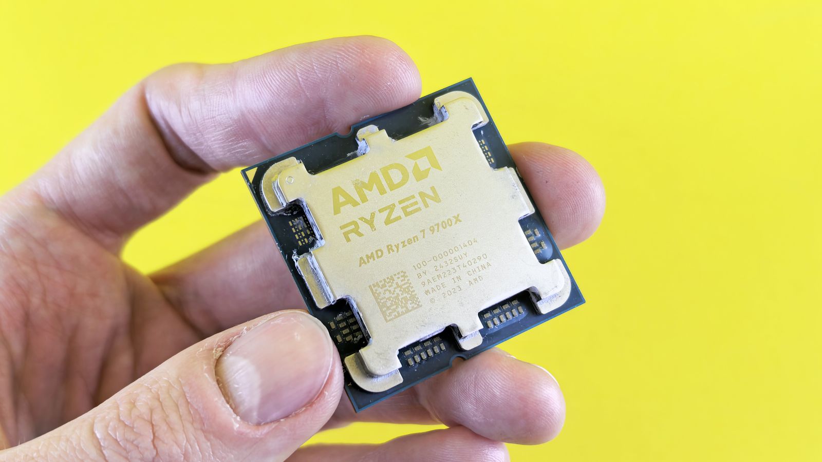 Detailed shot of AMD Ryzen 7 9700X processor held against bright yellow background.