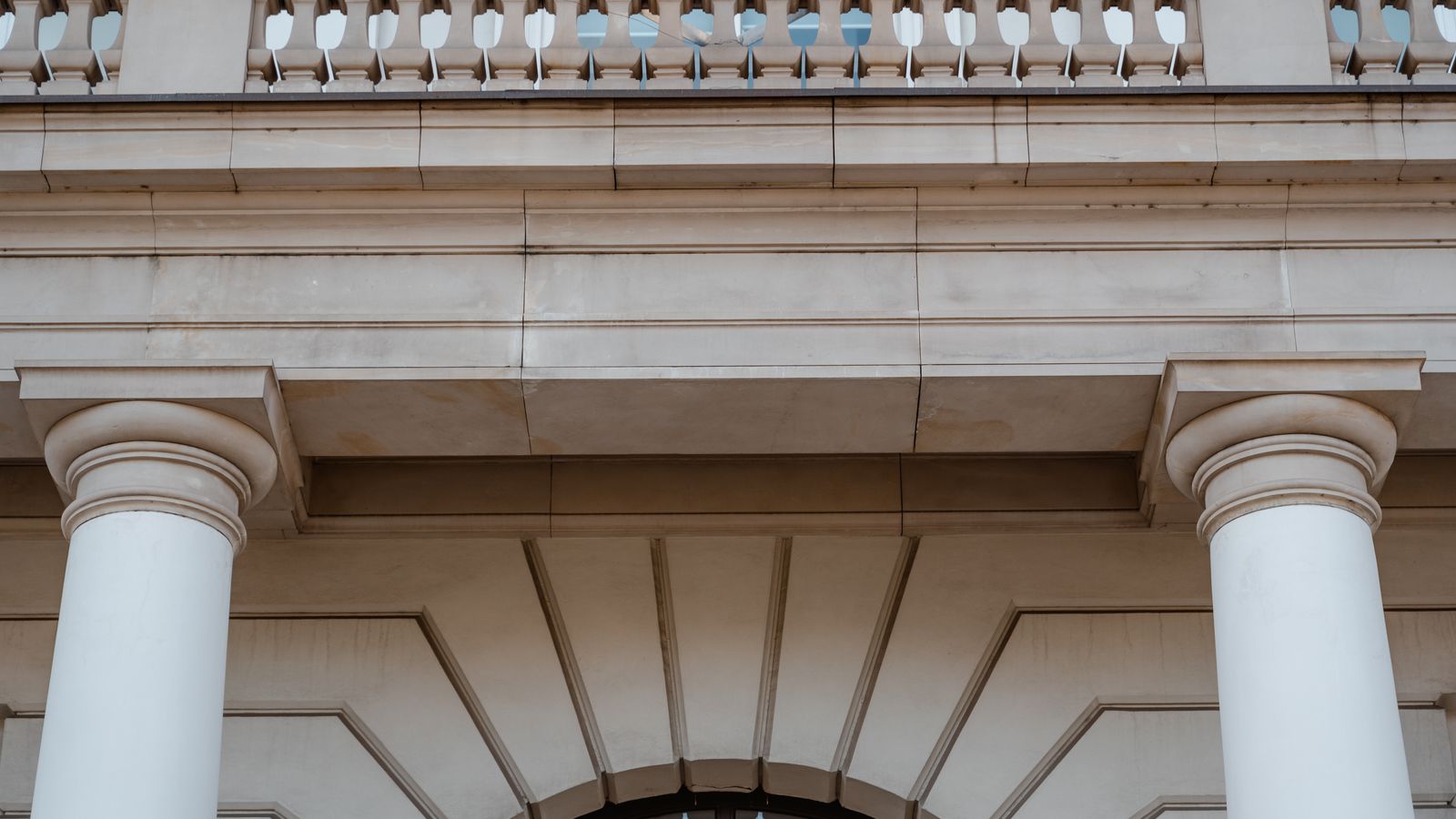 Low angle view of a neoclassical building facade featuring pillars and a balcony in daylight.