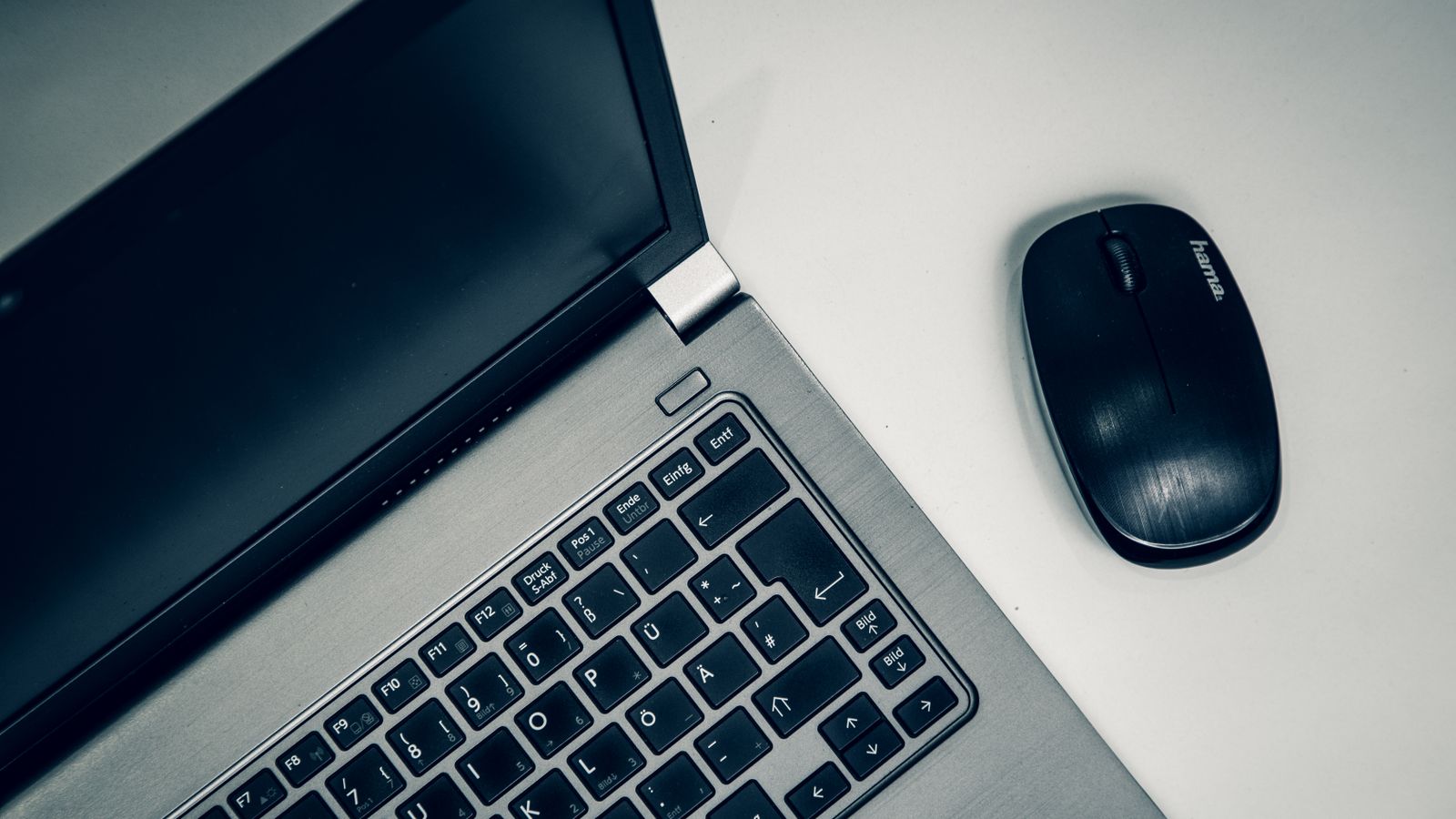 Close-up of a silver laptop and black wireless mouse on a white desk.