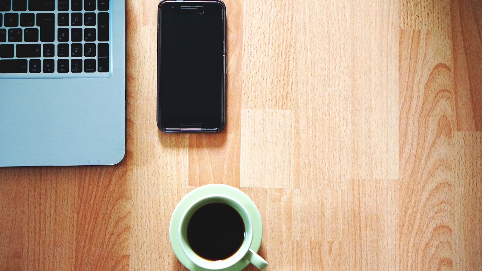 A tidy workspace with a laptop, smartphone, and coffee cup on a wooden desk.